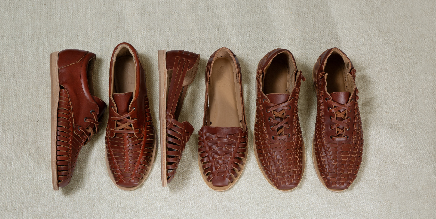 Six brown leather shoes and sandals are arranged in a row on a light beige textured fabric background, showing different styles and textures including woven, croc-embossed, and slotted designs.